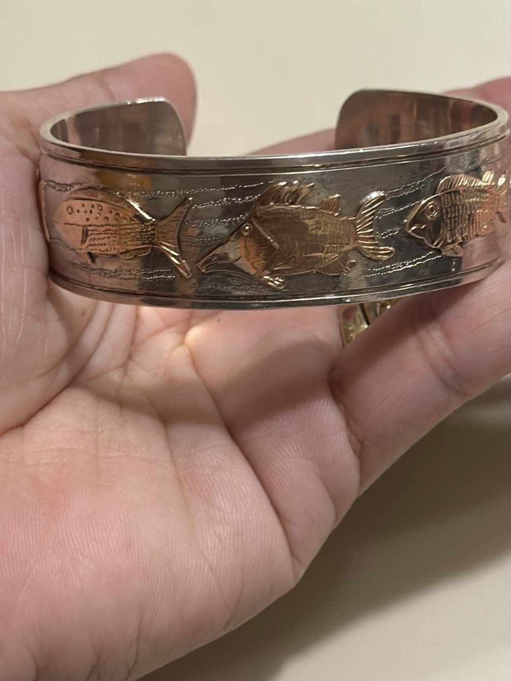 cuff bracelet features raised 14k gold  fish motifs set against sterling silver